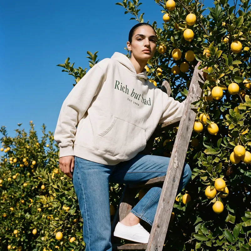 Yasmin on an orchard ladder in the cream Rich But Sad hoodie