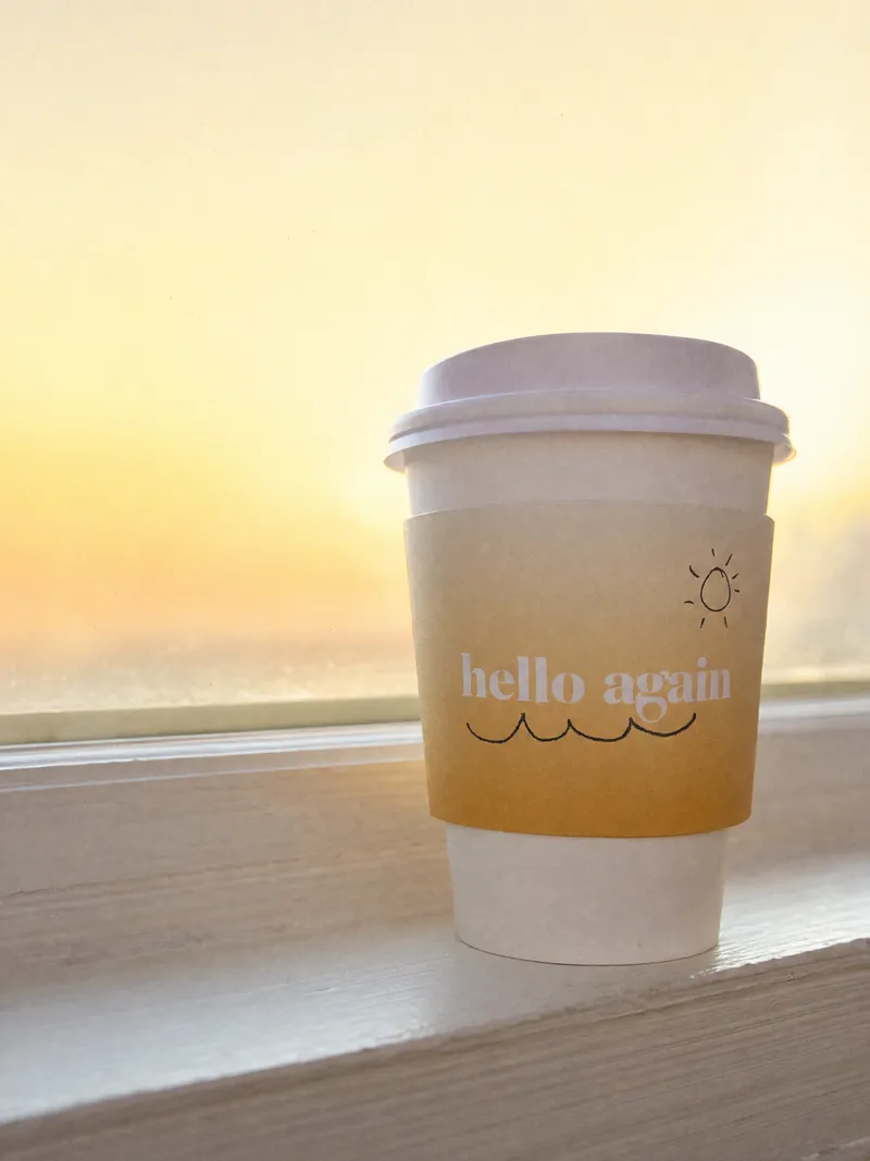 The cup on a white windowsill at dawn, the sky gold behind it