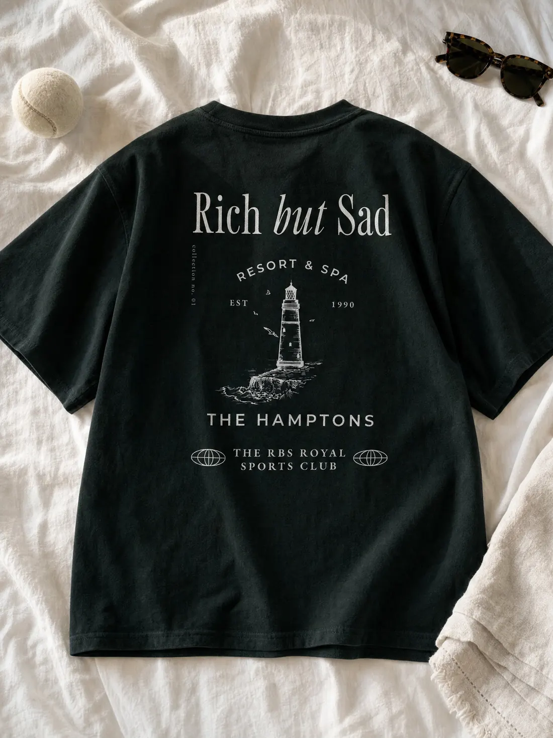 A forest green Rich But Sad tee laid flat on white linen